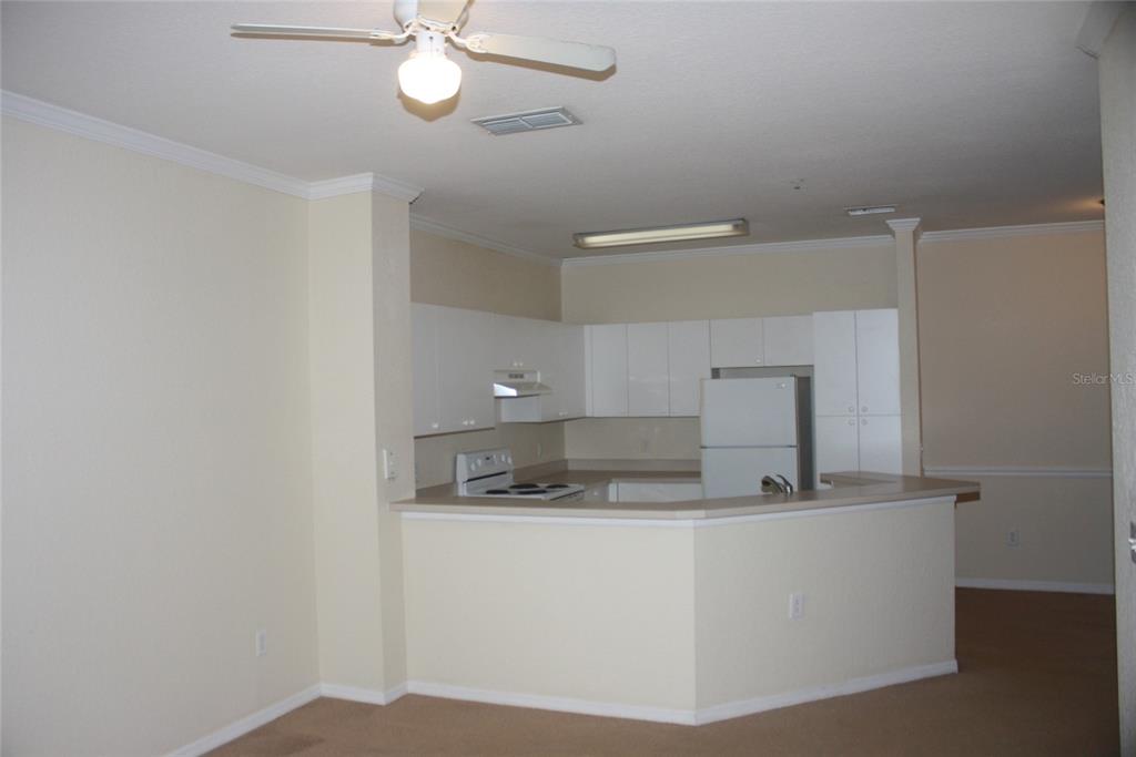 A kitchen with white cabinets and appliances features a breakfast bar overlooking a carpeted room — 3561 CONROY ROAD UNIT 234, ORLANDO, FL