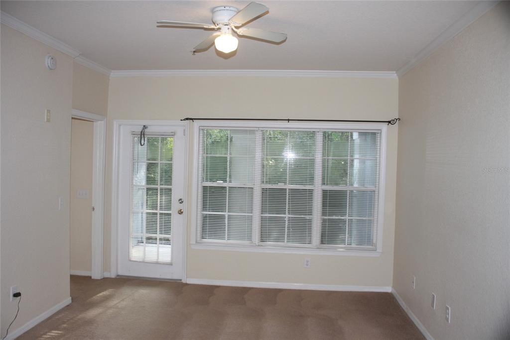 An empty room features beige carpet, a ceiling fan, a glass-paneled door, and large windows — 3561 CONROY ROAD UNIT 234, ORLANDO, FL