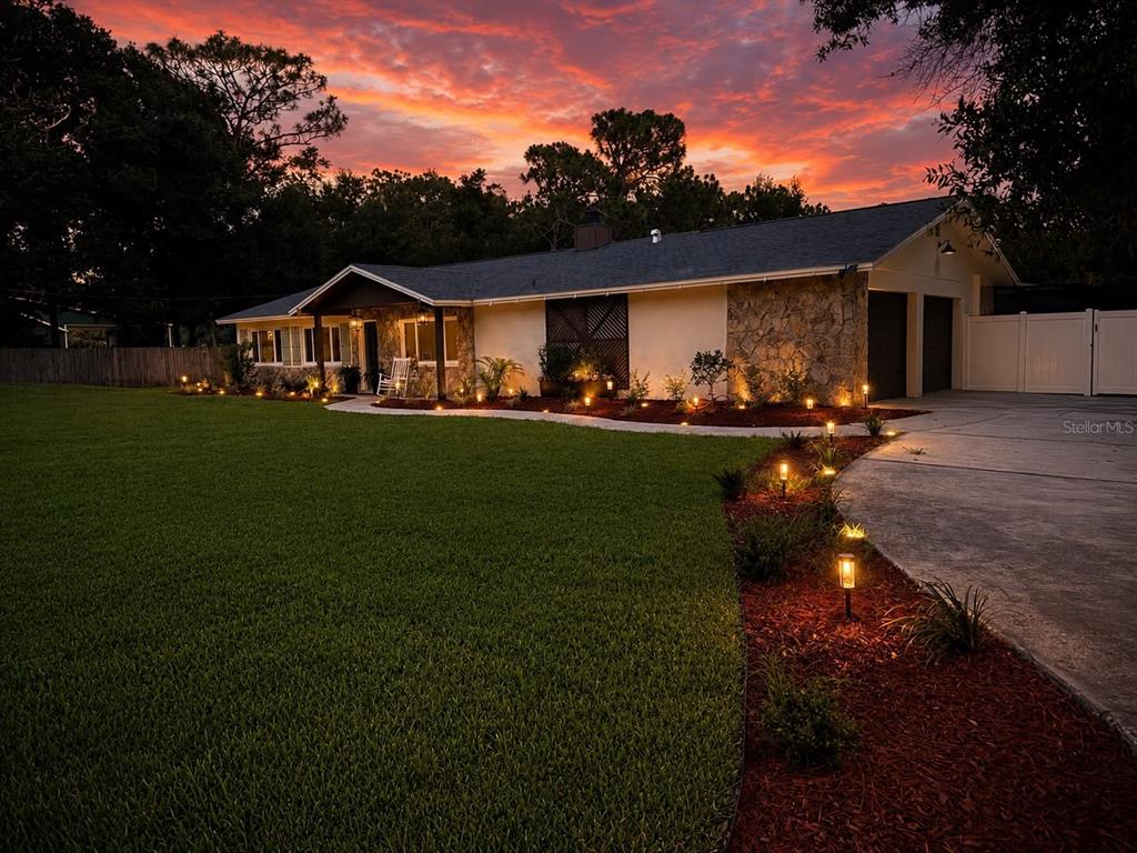 A single-story house with a stone facade and illuminated landscaping at sunset — 17238 BRIDLEPATH COURT, LUTZ, FL
