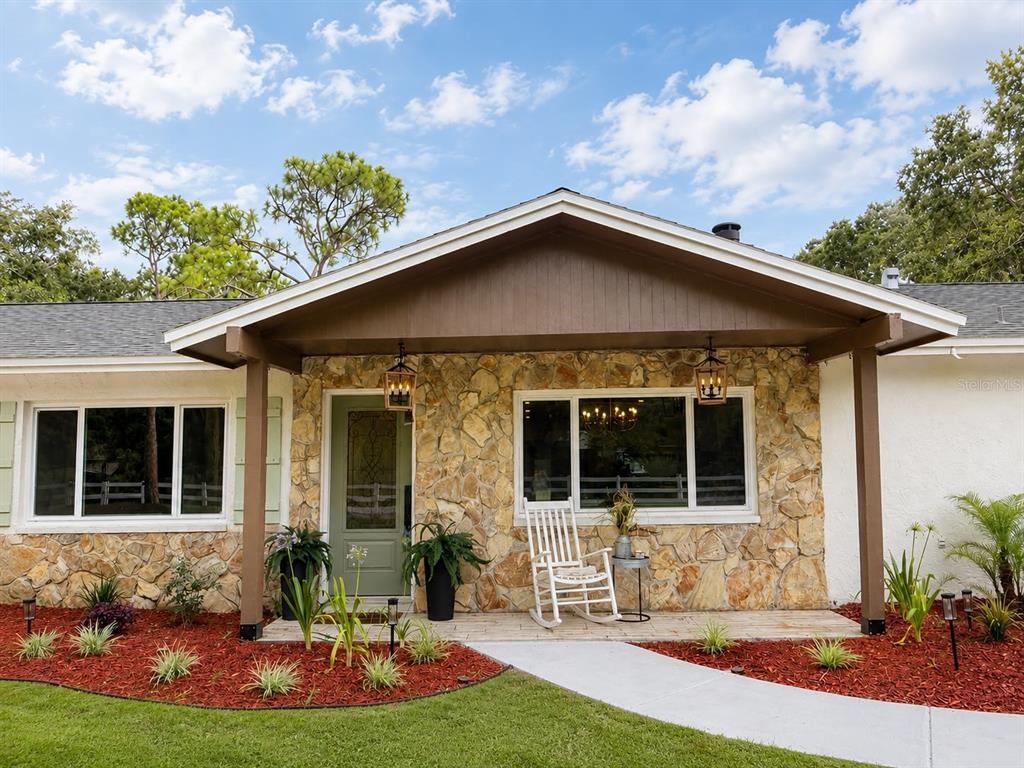 A single-story house exterior features a stone facade, a covered porch, and a rocking chair — 17238 BRIDLEPATH COURT, LUTZ, FL