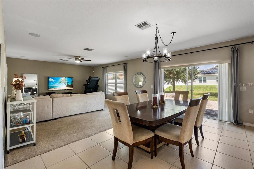 An open-concept living and dining area features tile flooring, a carpeted lounge, and sliding doors — 2226 TAYLOR CREEK COURT, KISSIMMEE, FL