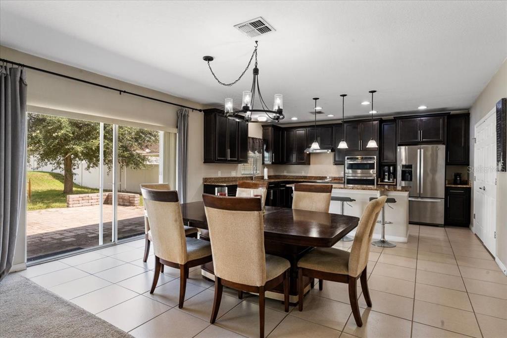 A dining area with a dark wood table and chairs opens to a kitchen with dark cabinets — 2226 TAYLOR CREEK COURT, KISSIMMEE, FL