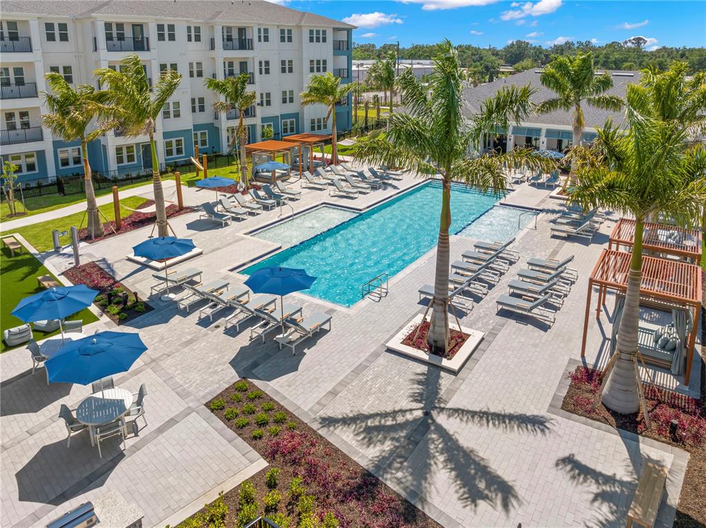 An outdoor swimming pool area features lounge chairs, blue umbrellas, and palm trees — 9720 BEAMING ROAD UNIT B2, VENICE, FL