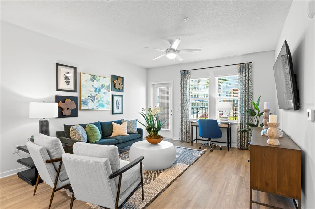 A living room features a blue sofa, two gray armchairs, a desk, and wood flooring — 9720 BEAMING ROAD UNIT B2, VENICE, FL