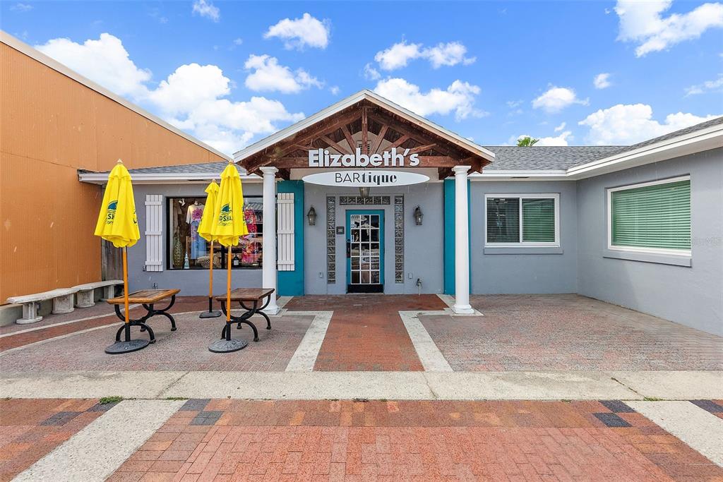 The exterior of a boutique storefront features a covered entrance, yellow umbrellas, and brick pavers — 350 COREY AVENUE, ST PETE BEACH, FL