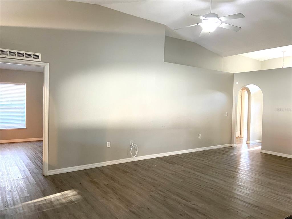 An empty living room features light gray walls, wood-look flooring, and a vaulted ceiling — 10459 FLY FISHING STREET, RIVERVIEW, FL