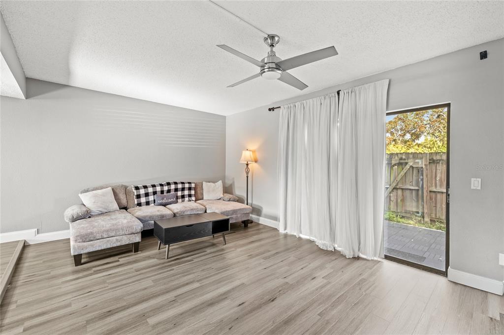 A living room with light wood-look flooring, a gray sectional sofa, and a sliding glass door — 707 SAINT MATTHEW CIRCLE, ALTAMONTE SPRINGS, FL