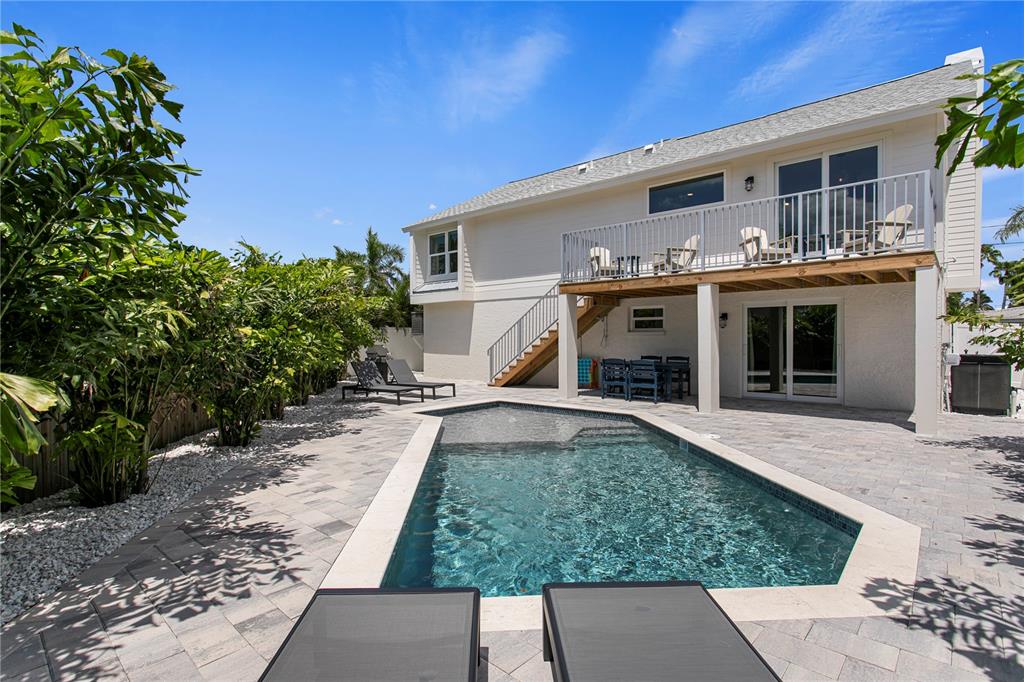 A backyard features a swimming pool, stone patio, elevated deck, and a two-story white house — 503 JANICE PLACE, INDIAN ROCKS BEACH, FL