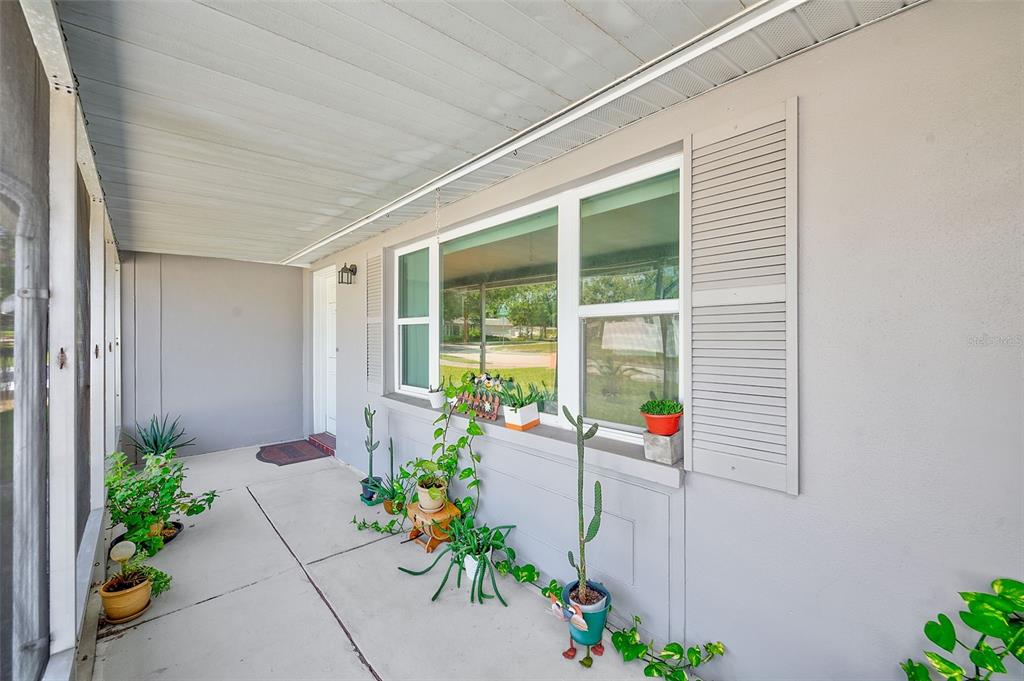 A covered porch features a concrete floor, a large window with shutters, and several potted plants — 5126 ROSEWOOD DRIVE, NEW PORT RICHEY, FL