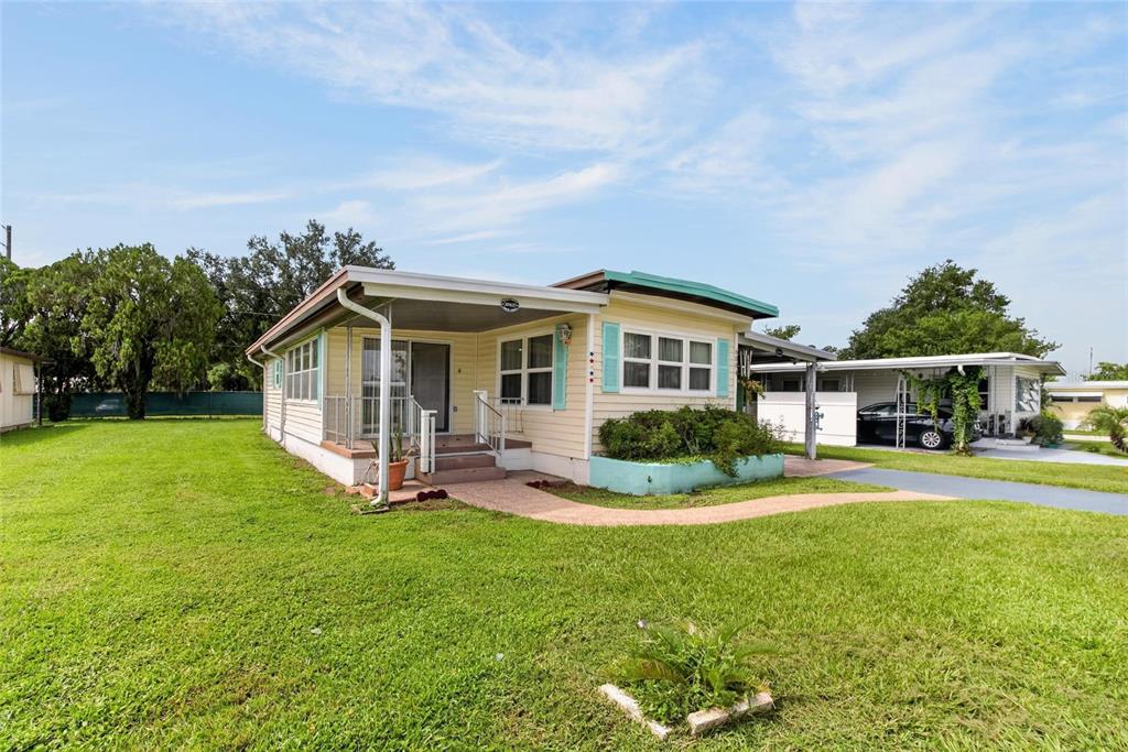 A light yellow mobile home with a covered front porch and a turquoise planter box — 6004 ALPINE DRIVE, ZEPHYRHILLS, FL