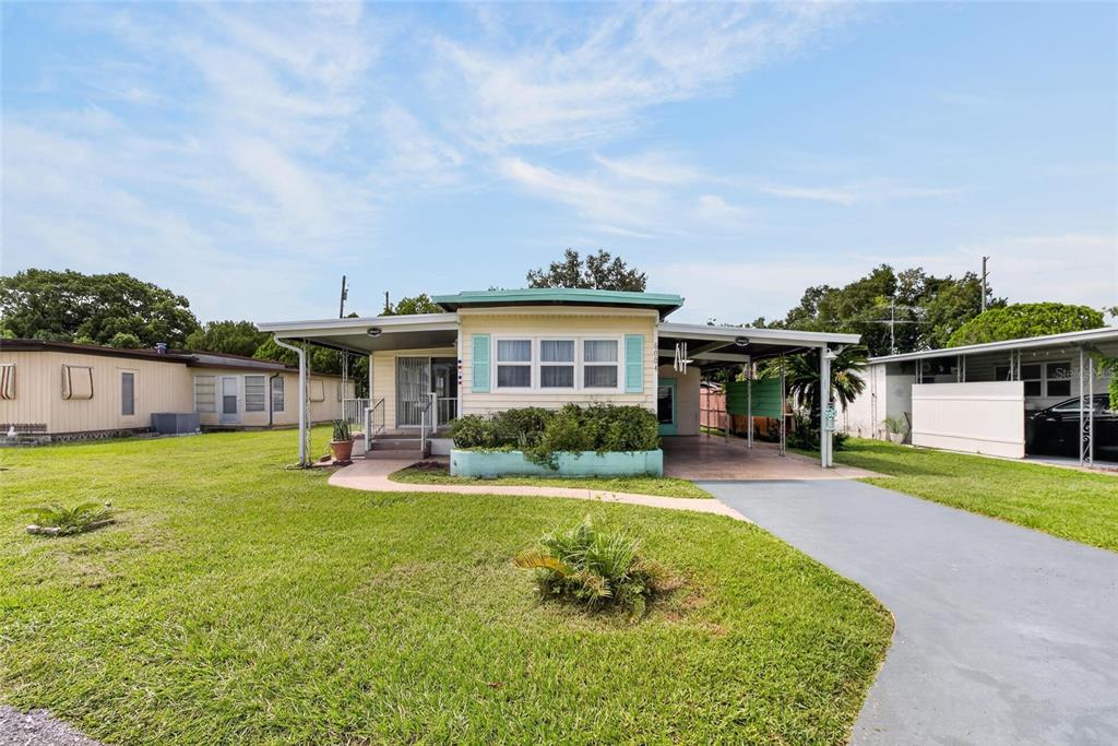 A single-story mobile home with a carport and a front lawn under a blue sky — 6004 ALPINE DRIVE, ZEPHYRHILLS, FL