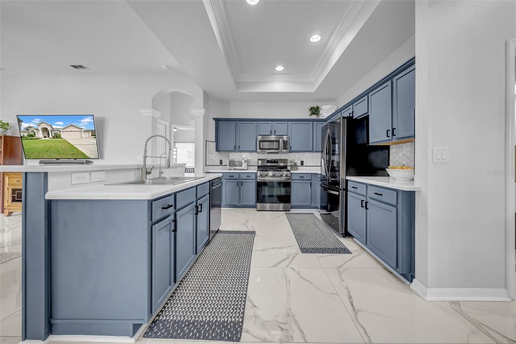 A kitchen features blue cabinets, white countertops, stainless steel appliances, and white marble-look tile flooring — 4455 GEVALIA DRIVE, BROOKSVILLE, FL