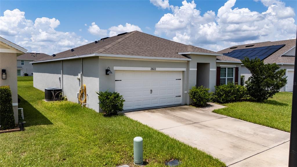 A single-story house with a white garage door, a concrete driveway, and a grassy yard — 2822 HARMONIA HAMMOCK RD, HARMONY, FL
