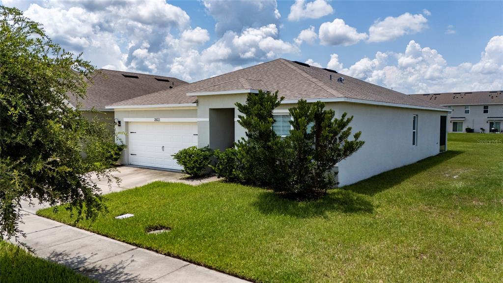 A single-story house with a white garage, tan stucco exterior, and a green lawn — 2822 HARMONIA HAMMOCK RD, HARMONY, FL