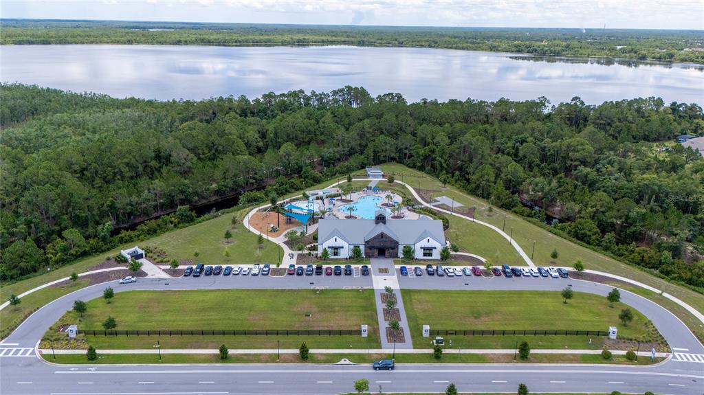 An aerial view shows a community clubhouse with a swimming pool, parking lot, and lake — 2822 HARMONIA HAMMOCK RD, HARMONY, FL
