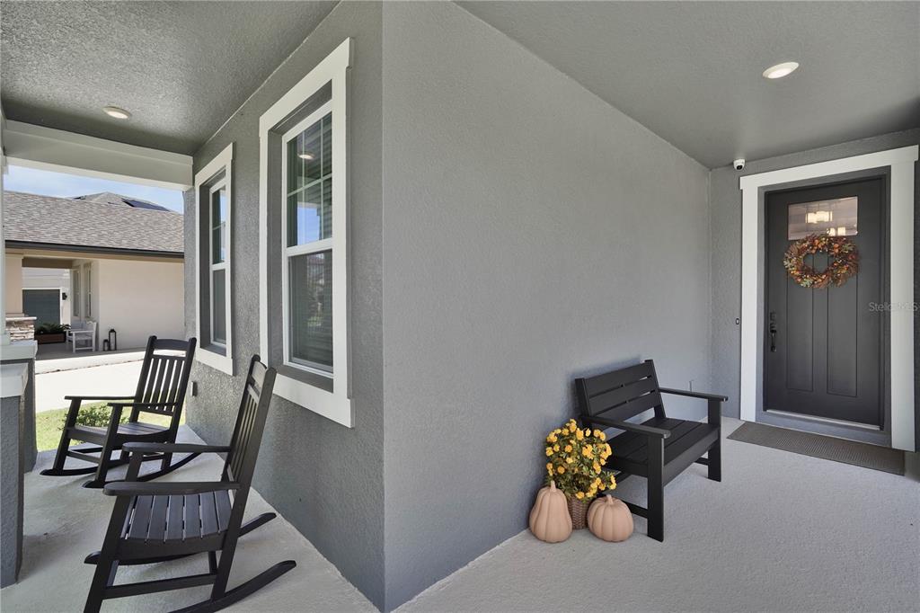 A covered front porch features gray walls, a dark front door, and black outdoor seating — 2210 GOLD DUST DRIVE, MINNEOLA, FL