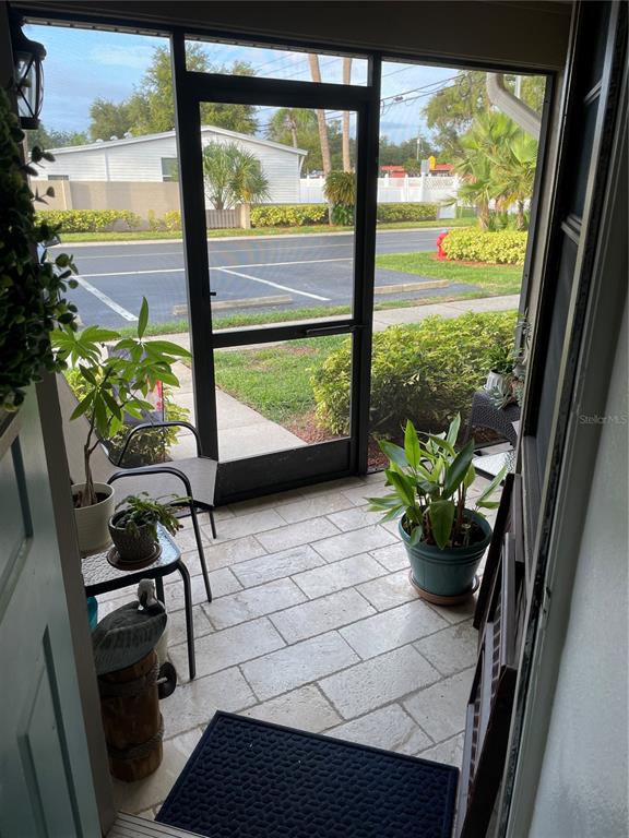A screened-in porch features light-colored stone flooring, several potted plants, and a view of a parking lot — 2131 RIDGE ROAD S UNIT 2, LARGO, FL