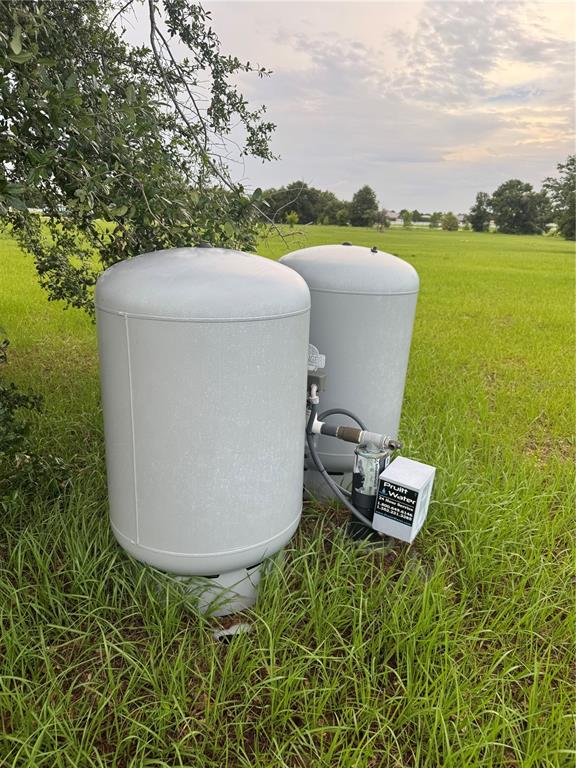 Two large grey water pressure tanks sit in a grassy field under a tree — GROVES DRIVE, GROVELAND, FL