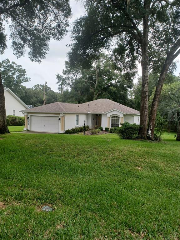 A single-story house with a white stucco exterior, a two-car garage, and mature trees — 19199 SW 92ND LOOP, DUNNELLON, FL