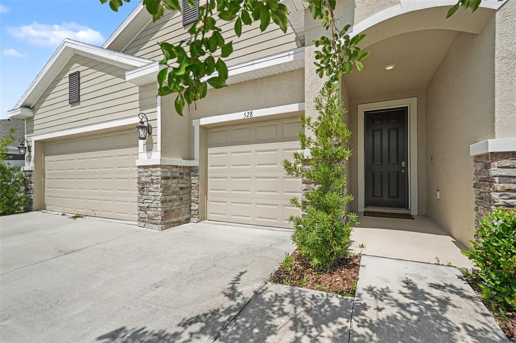 A two-car garage home with stone accents, beige siding, and a dark front door — 528 OCEAN SPRAY DRIVE, RUSKIN, FL