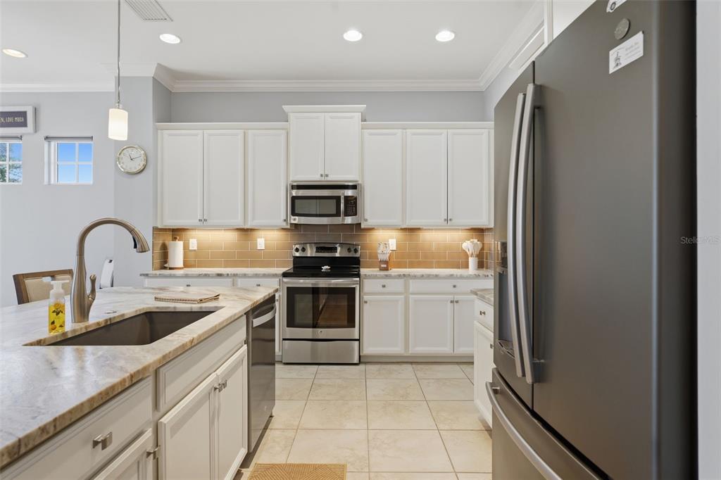 A kitchen features white cabinets, stainless steel appliances, a marble-topped island, and a tiled backsplash — 10311 LANDS END CIRCLE UNIT 13, PLACIDA, FL