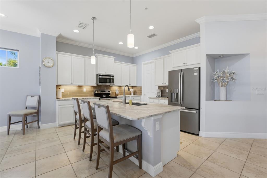 A kitchen features white cabinets, a stone-topped island with bar seating, and stainless steel appliances — 10311 LANDS END CIRCLE UNIT 13, PLACIDA, FL