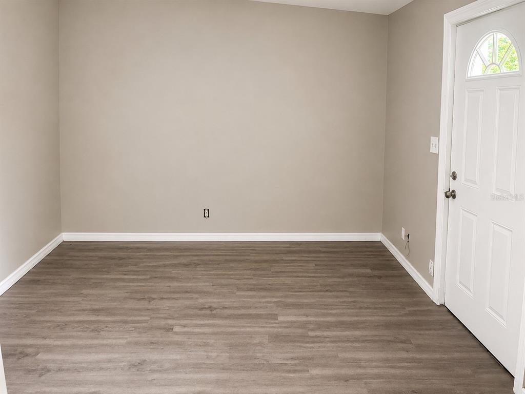 An empty room features light gray walls, wood-look vinyl flooring, and a white entry door — 16 N CHRISTIANA AVENUE, APOPKA, FL