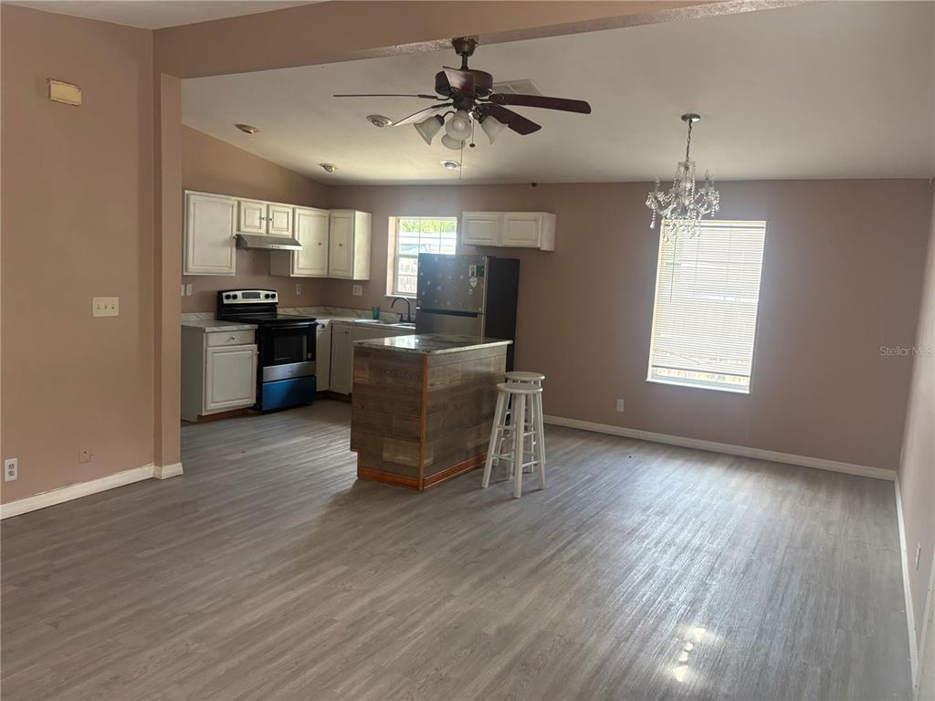 A kitchen with white cabinets, a wood-paneled island, and gray flooring opens to a dining area — 16 N CHRISTIANA AVENUE, APOPKA, FL