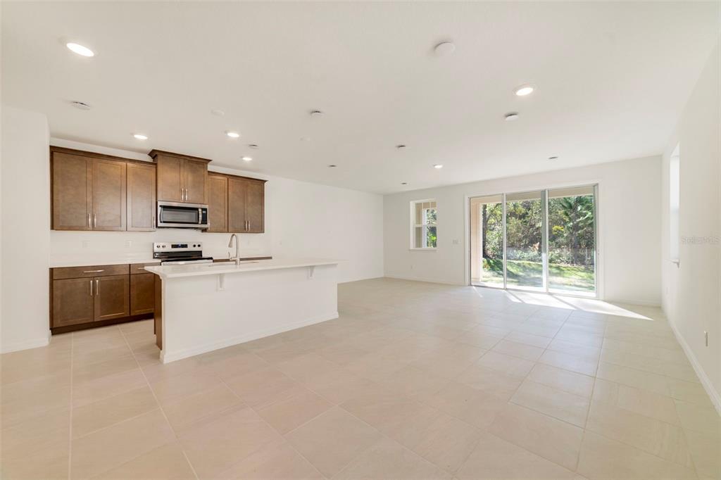 A kitchen with dark wood cabinets and a white island opens into a spacious living area — 1669 GREENLEAF WOODS COVE, OVIEDO, FL