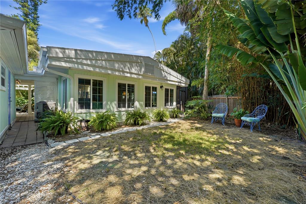 A light green house exterior with a grassy yard, patio furniture, and lush tropical landscaping — 3424 OLD OAK DRIVE, SARASOTA, FL