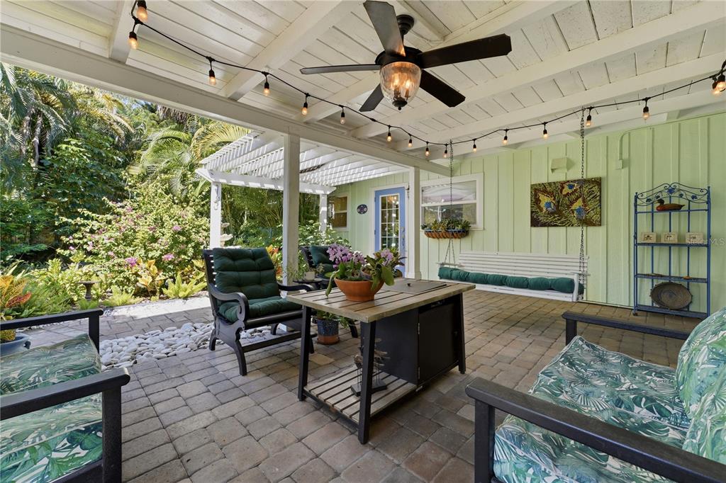A covered patio features a fire pit table, outdoor seating, string lights, and a hanging bench — 3424 OLD OAK DRIVE, SARASOTA, FL