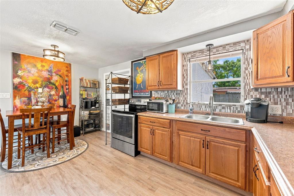 A kitchen with wood cabinets, stainless steel appliances, a dining area, and a mosaic backsplash — 3607 LATIMER STREET, NEW PORT RICHEY, FL