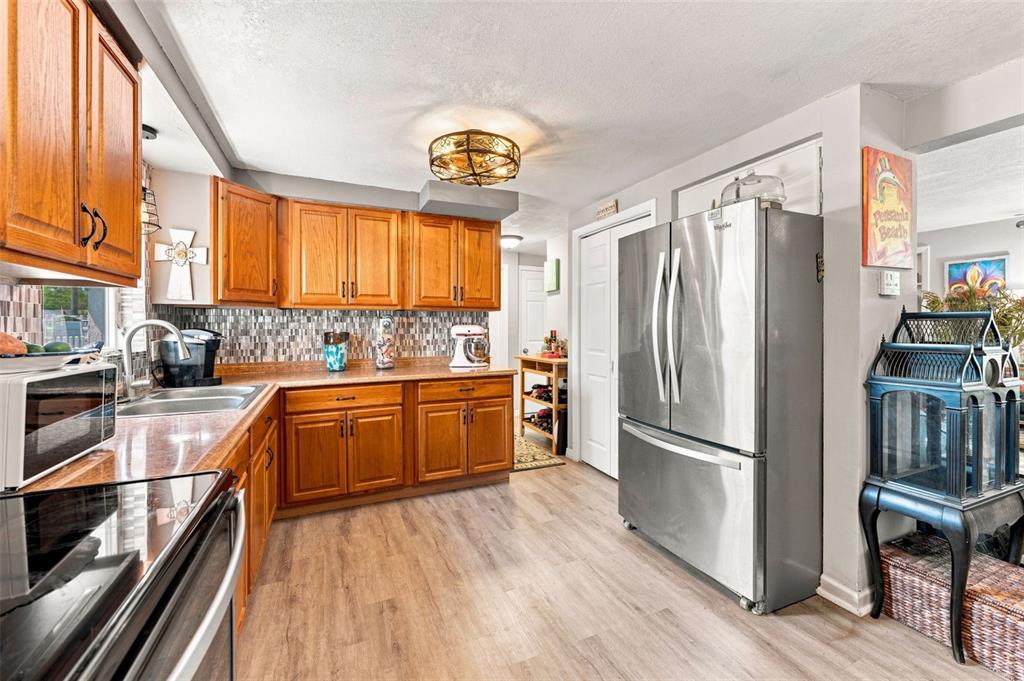 A kitchen features wood cabinets, stainless steel appliances, a tiled backsplash, and light wood flooring — 3607 LATIMER STREET, NEW PORT RICHEY, FL