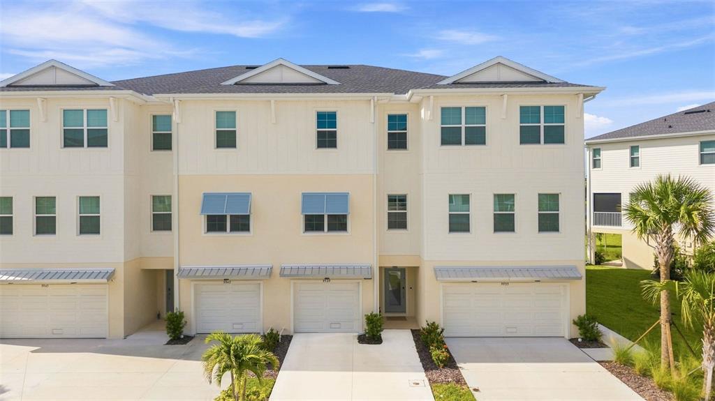 A three-story townhouse exterior features light-colored siding, multiple garage doors, and a palm tree — 9939 KEY HAVEN ROAD, SEMINOLE, FL