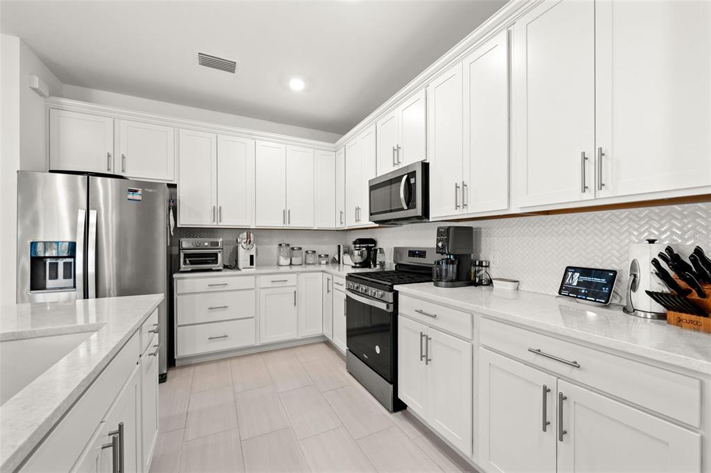 A modern kitchen features white cabinets, stainless steel appliances, and light-colored quartz countertops — 12461 BASALT LANE, ALVA, FL