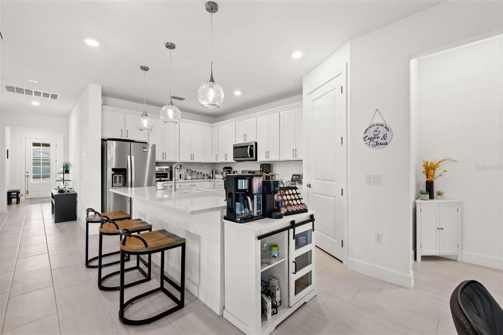 A modern kitchen features white cabinetry, a large island with bar seating, and stainless appliances — 12461 BASALT LANE, ALVA, FL