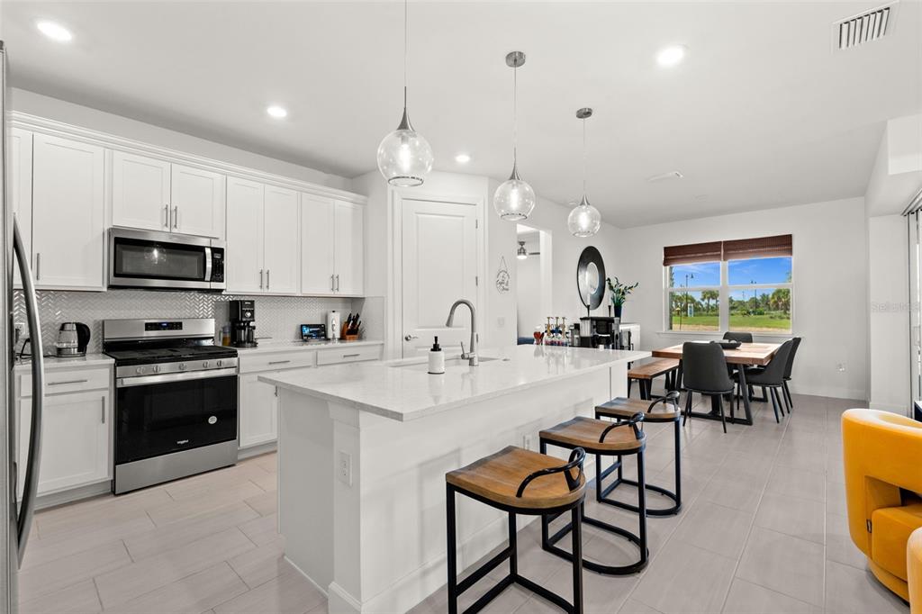 A modern kitchen features white cabinetry, a central island with bar seating, and stainless appliances — 12461 BASALT LANE, ALVA, FL