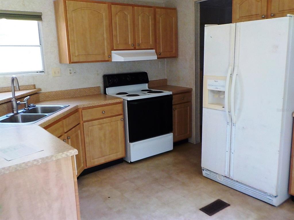 A kitchen features light wood cabinets, laminate countertops, a white stove, and a white refrigerator — 7398 SW NORMAC DRIVE, ARCADIA, FL