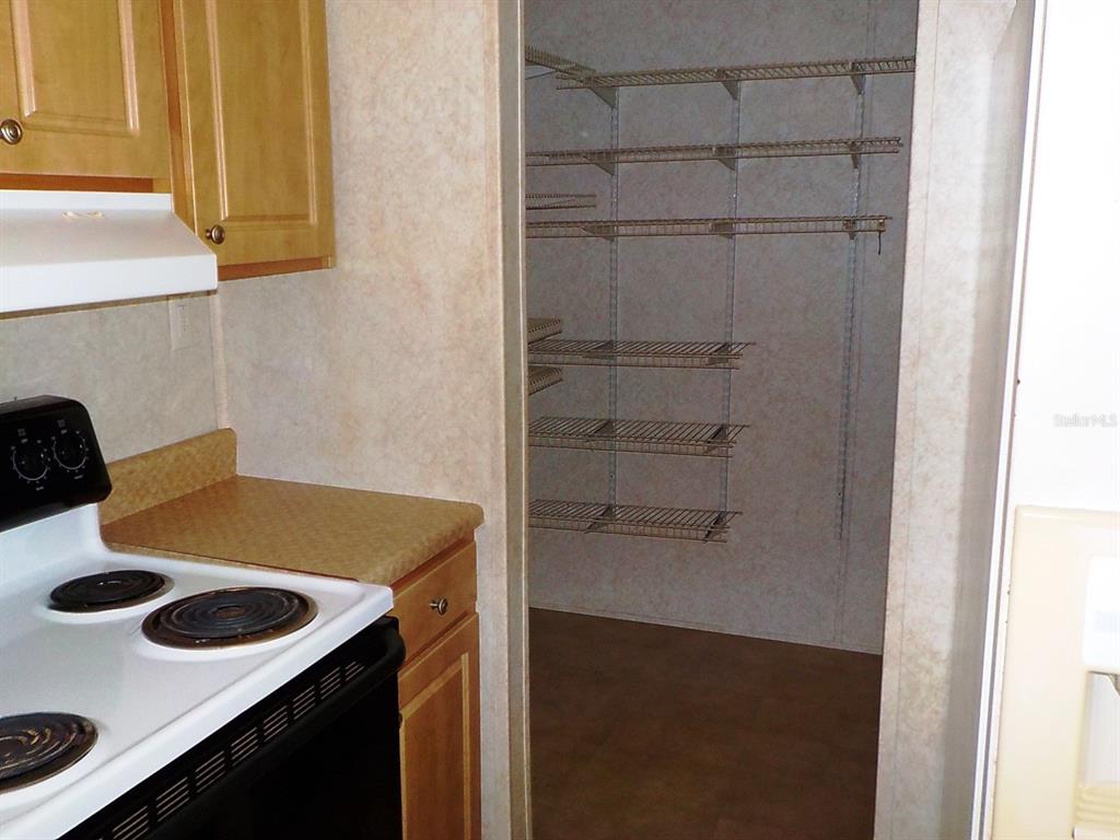 A kitchen with a white stove and wooden cabinets next to an open pantry — 7398 SW NORMAC DRIVE, ARCADIA, FL
