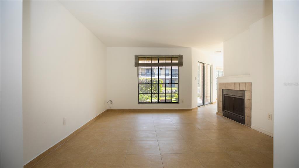 An empty living room features beige tile flooring, a fireplace, and a large window — 8711 FANCY FINCH DRIVE UNIT 101, TAMPA, FL