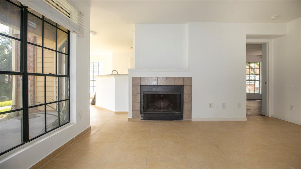 A living room features a tiled fireplace, beige floor tiles, and a large window — 8711 FANCY FINCH DRIVE UNIT 101, TAMPA, FL