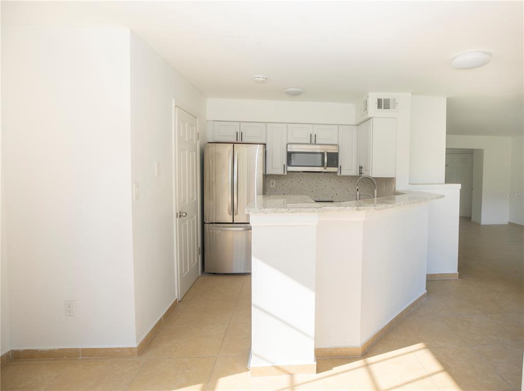 A kitchen features white cabinetry, stainless steel appliances, and a breakfast bar with stone countertops — 8711 FANCY FINCH DRIVE UNIT 101, TAMPA, FL