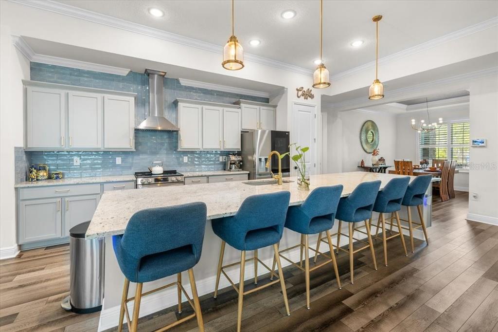A kitchen with light gray cabinets, blue tile backsplash, and a large island with barstools — 7 BELLIS COURT, HOMOSASSA, FL