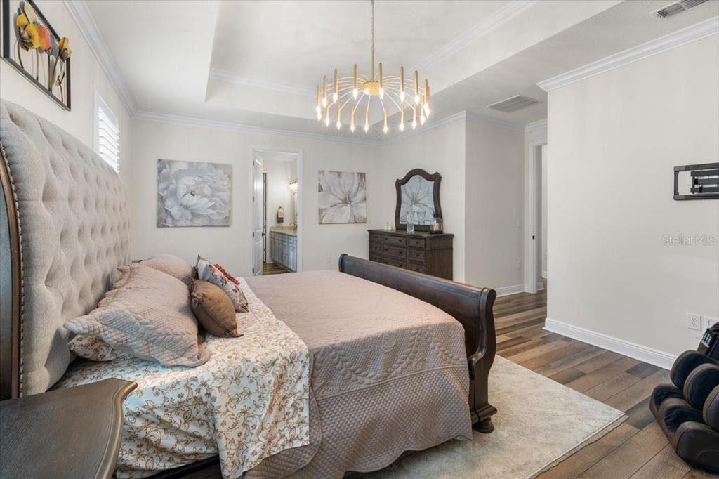 A bedroom features a tufted headboard, a modern chandelier, and wood-look flooring — 7 BELLIS COURT, HOMOSASSA, FL