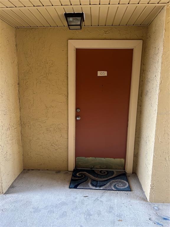 A red apartment door numbered 105 is set within a textured beige exterior wall — 636 KENWICK CIRCLE UNIT 105, CASSELBERRY, FL
