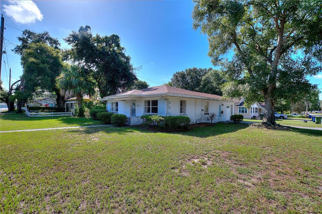 A single-story white house with a hip roof sits on a grassy corner lot — 708 AVENUE E NE, WINTER HAVEN, FL