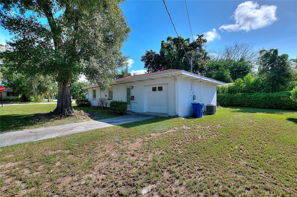 A white single-story house with a garage and a large tree in the front yard — 708 AVENUE E NE, WINTER HAVEN, FL