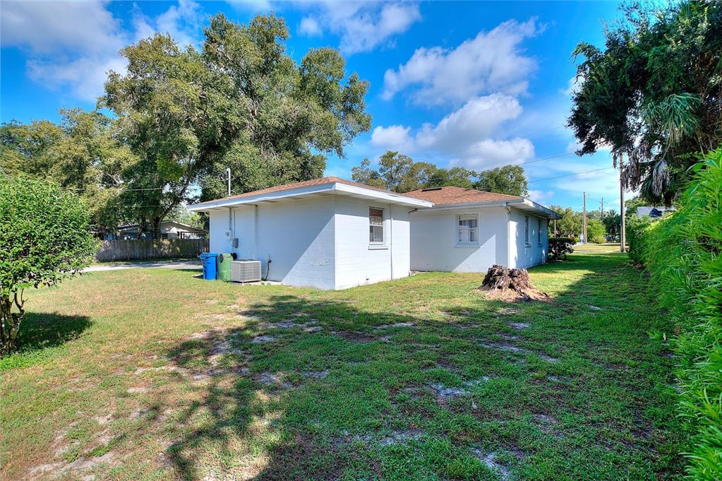 A white, single-story house with a flat roof sits on a grassy lot with trees — 708 AVENUE E NE, WINTER HAVEN, FL