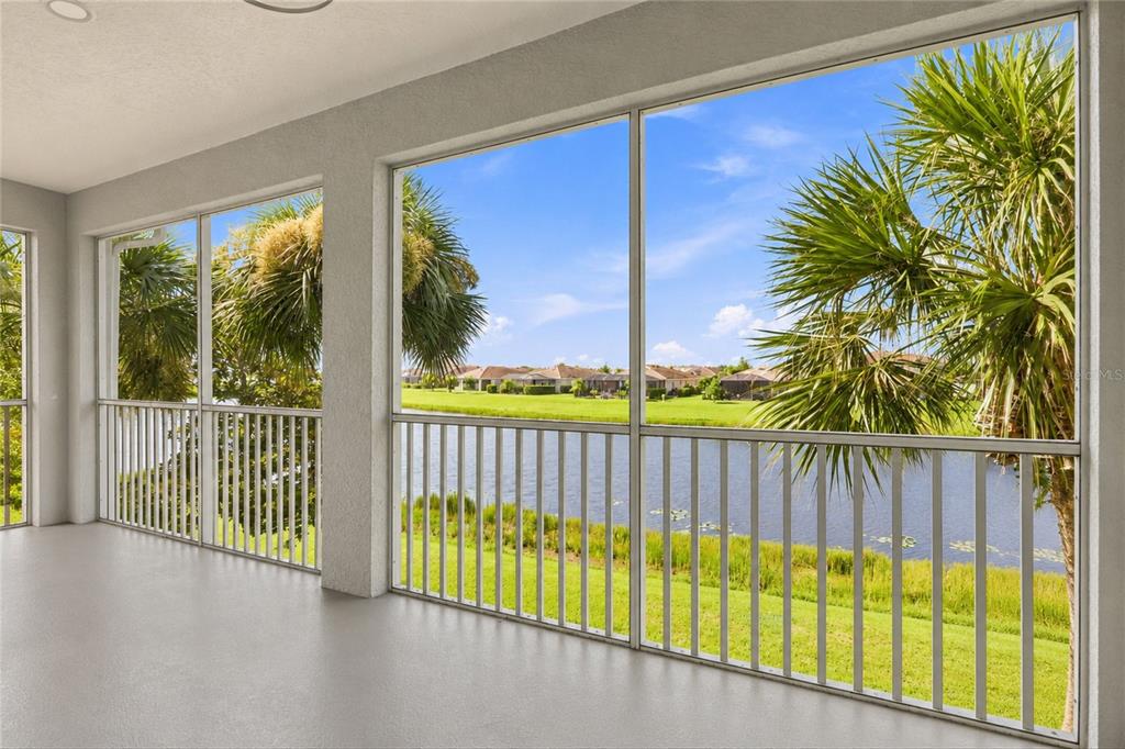 A screened-in patio with light gray flooring overlooks a lake and residential neighborhood — 16560 GOLDENROD LANE UNIT 201, ALVA, FL