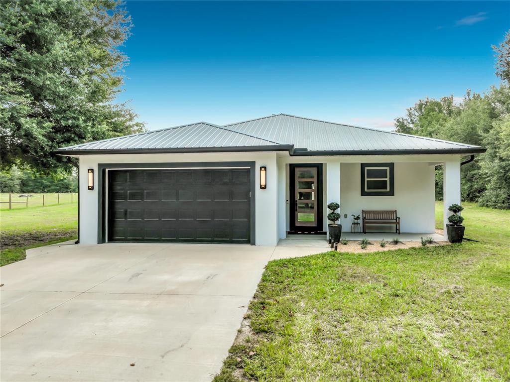 A single-story house with a metal roof, white stucco exterior, and a black garage door — 34814 WILLIAM LANE, EUSTIS, FL